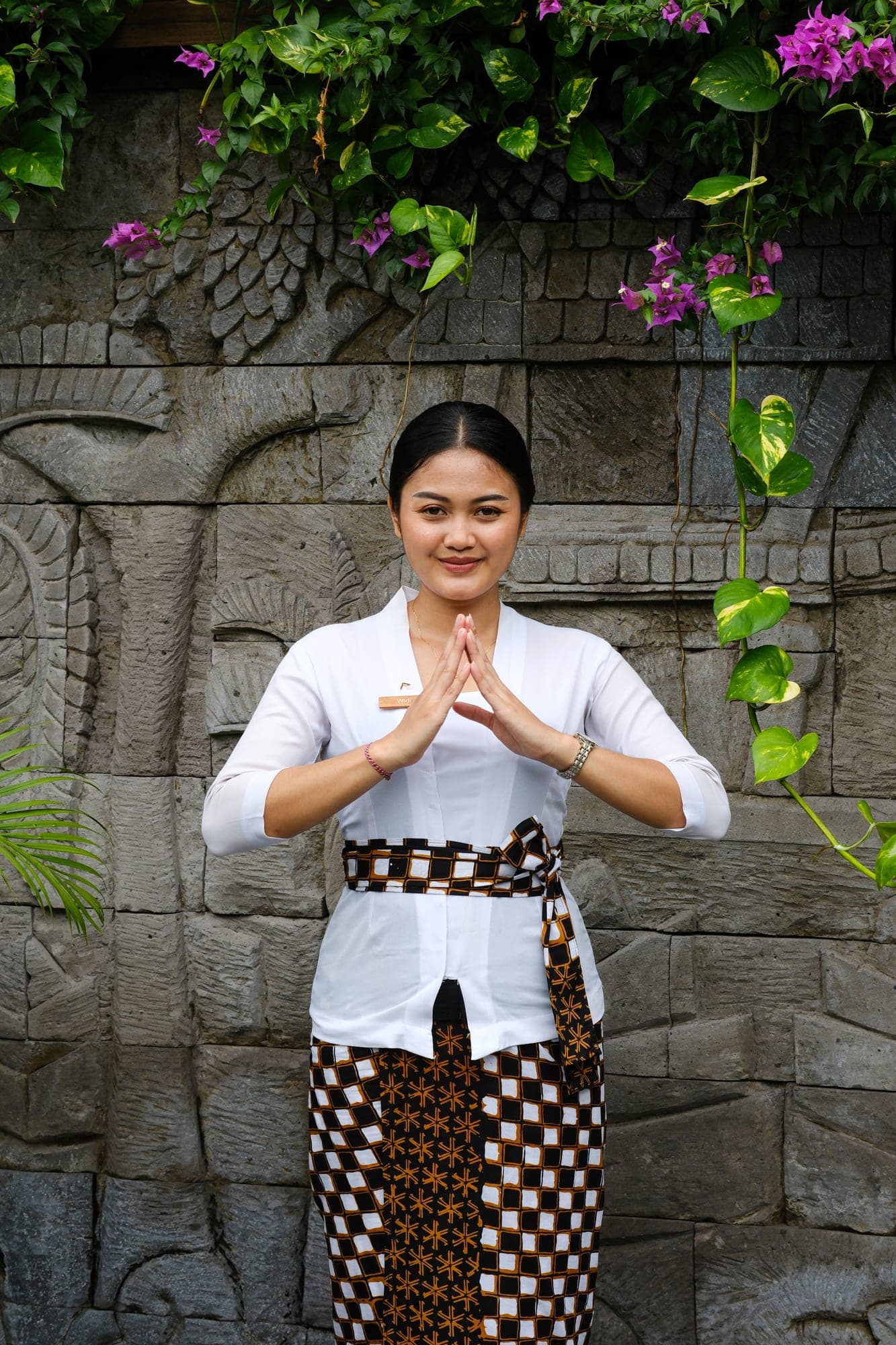 A host offering a Balinese welcome beside a carved stone wall