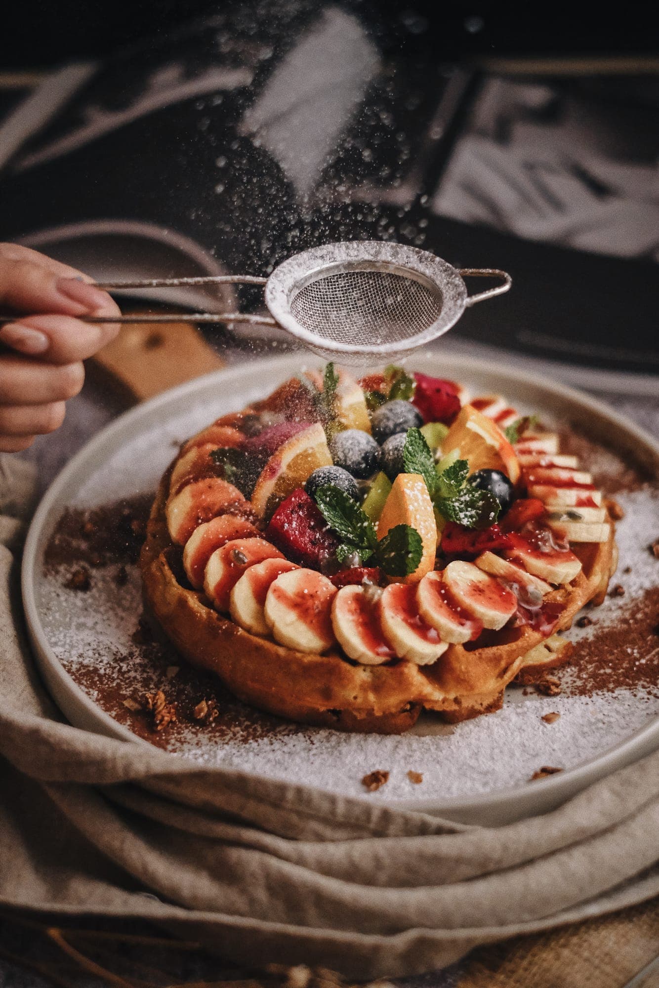 Icing sugar being dusted over a fruit tart during a food shoot