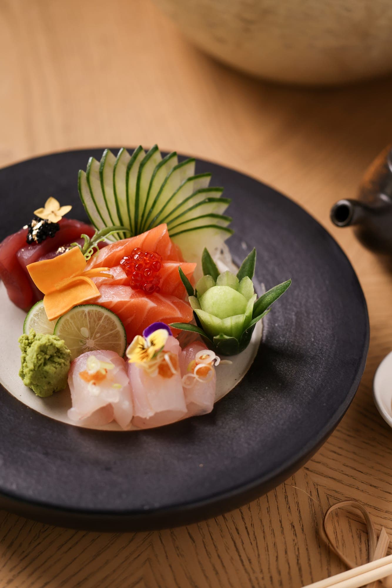 A sashimi platter with a cucumber fan on a dark plate