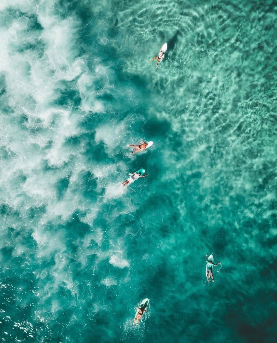 Surfers in turquoise water off the Bali coast, seen from above
