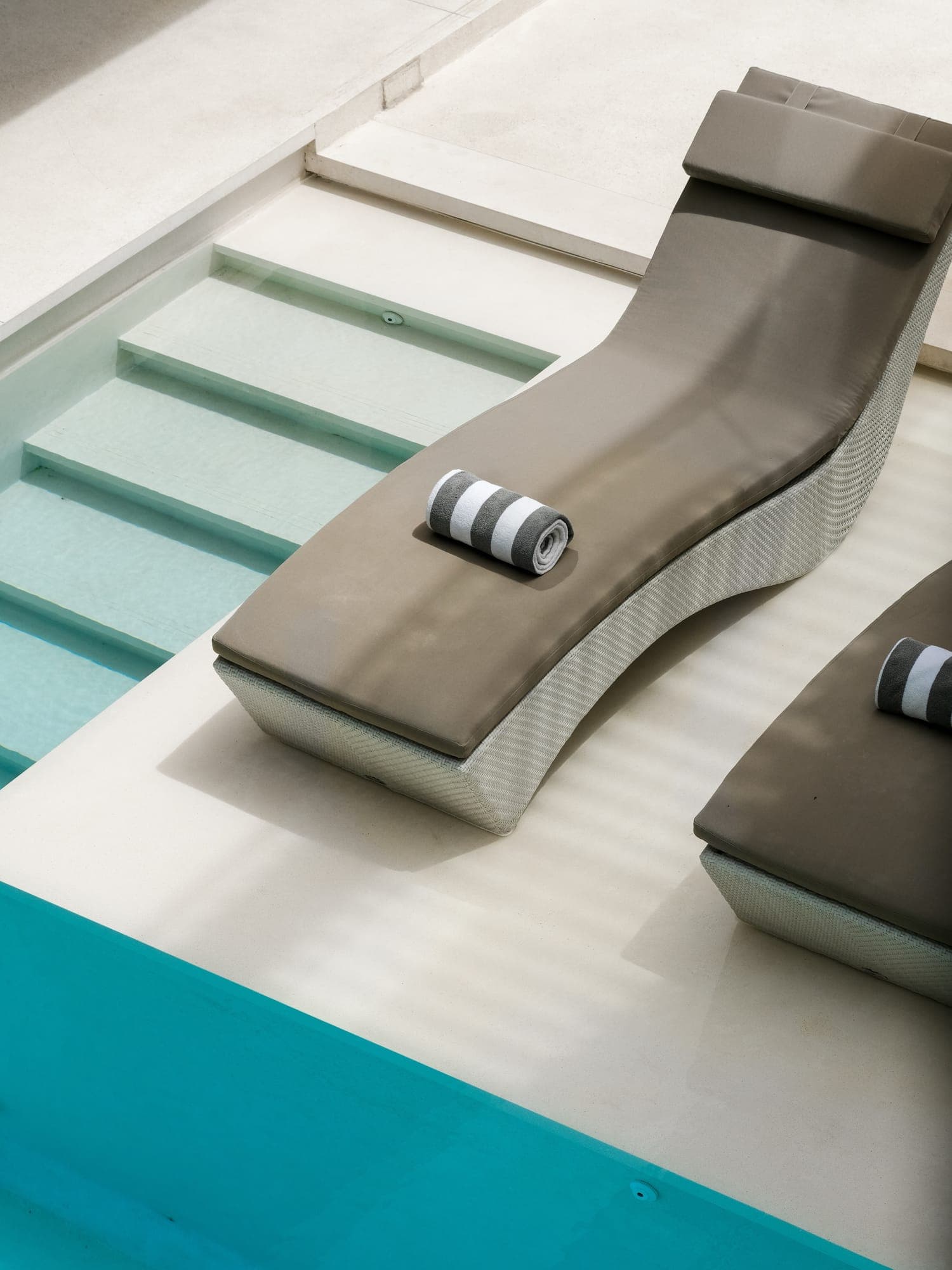 A sun lounger on the step of a turquoise villa pool