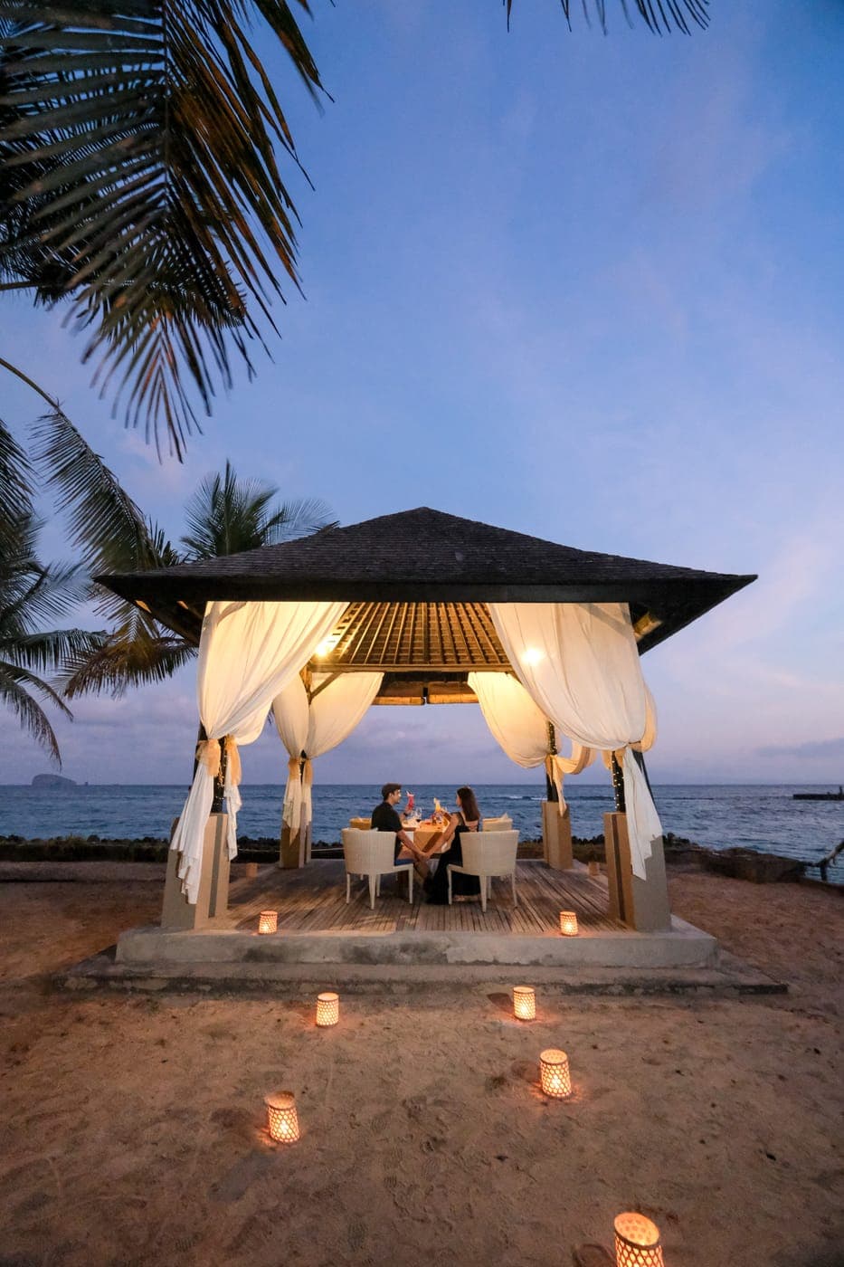 A candlelit gazebo dinner on the beach at dusk