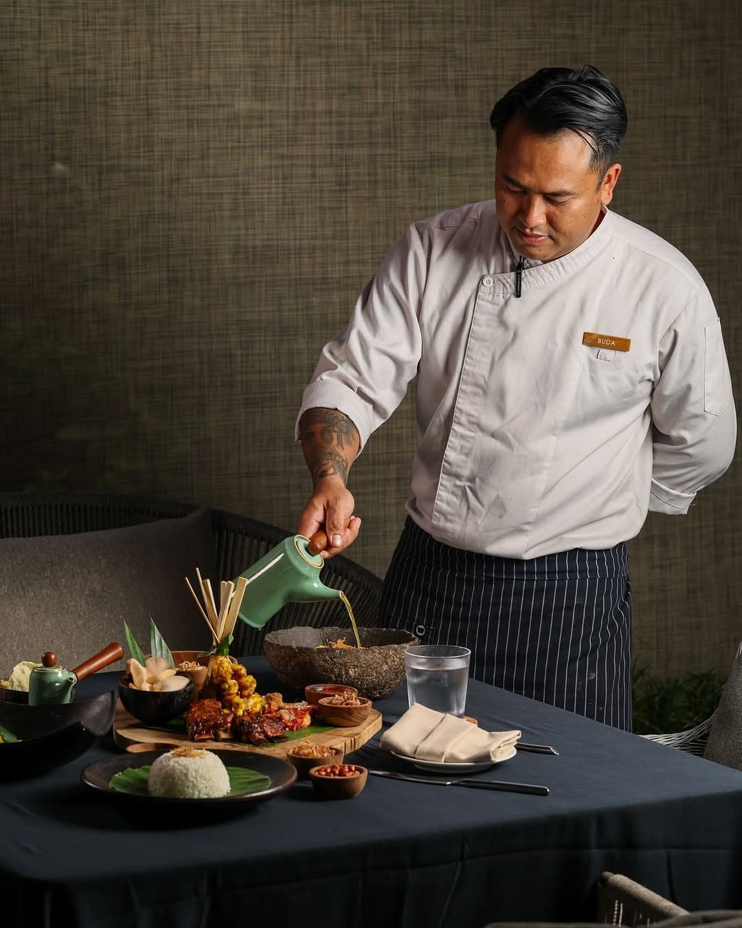 A chef pouring sauce over a table of Indonesian dishes